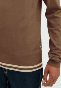 Pullover tricotat de culoare maro, cu manșete și tiv cu nervuri; are dungi crem. Materialul este moale, cu o textură netedă, evidențiind un design casual.