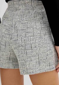 Pantalones cortos de tejido en un patrón de crema claro y negro, con una superficie texturizada y un dobladillo deshilachado. Diseño de cintura suave.