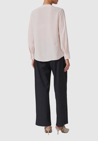 Blouse en satin rose clair à manches longues et poignets à boutons, associée à un pantalon large à rayures noires et blanches et des chaussures à talons hauts gris clair.