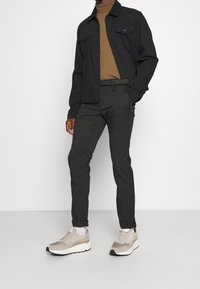 Mustat farkkutakki, jossa on turkisläntä, ruskea korkea kauluspaita, harmaat muotoillut housut ja beige kengät, joissa on sävyjä korostavia yksityiskohtia ja paksu pohja.