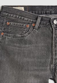 Jean en denim gris avec une texture délavée, rivets de couleur cuivre et bouton de fermeture standard ; comprend une poche à monnaie et des détails cousus.