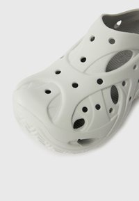 Gray lightweight clog made of soft material, featuring cut-out holes for ventilation, a textured upper, and a ridged sole for grip.