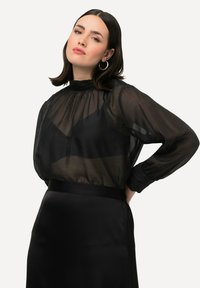 Transparante zwarte blouse met een hoge hals en pofmouwen, gecombineerd met een strakke zwarte rok. Soepele textuur en subtiele glans overal.