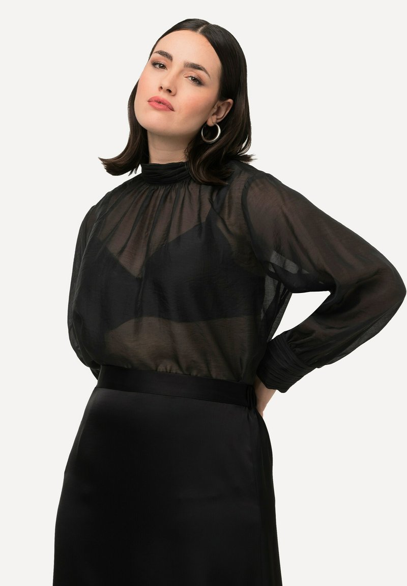 Transparante zwarte blouse met een hoge hals en pofmouwen, gecombineerd met een strakke zwarte rok. Soepele textuur en subtiele glans overal.