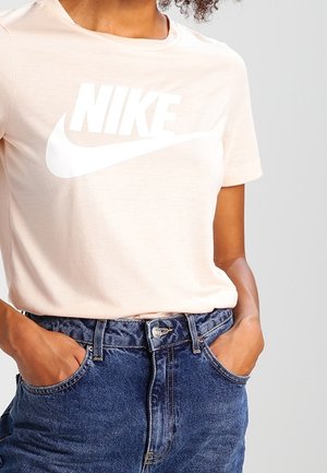 T-shirt Nike rose clair à manches courtes avec un grand logo blanc et un col rond, associé à un jean en denim bleu taille haute.