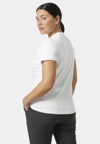 Camiseta de algodón blanca con mangas cortas, escote redondo y un corte relajado. Combinada con pantalones oscuros, que muestran una textura suave.