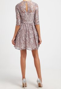 Spetsklänning med halv ärm, detalj med nyckelhål i ryggen och en utsvängd kjol i ljus mauve. Bärs med beige klackar med glittrande detaljer.