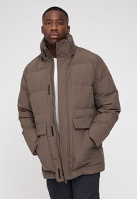 Braune Daunenjacke mit hohem Kragen, vertikalen Nähten, Frontreißverschluss, zwei Fronttaschen und schwarzen Akzenten. Texturiertes Material, lockere Passform.