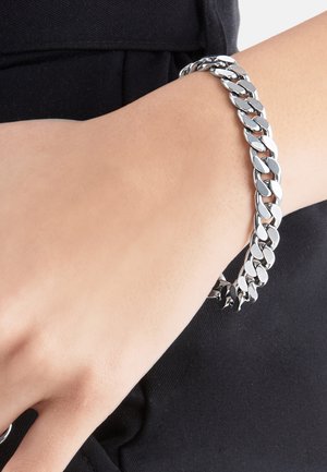 Silver chunky chain bracelet worn on wrist against black fabric background.