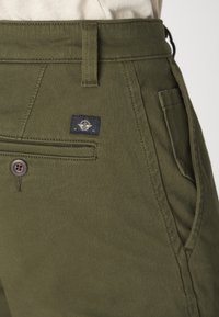 Pantalons vert olive en toile de coton, dotés d'une poche avant, d'une taille cousue et d'un petit logo de la marque bleu marine sur le côté.