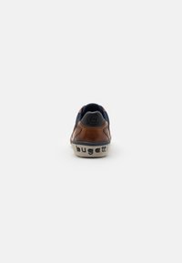 Brown leather sneaker with navy accents, rounded shape, contrasting textured sole, and "bugatti" branding on the heel.