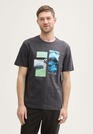 Camiseta de algodón gris con un estampado gráfico que presenta imágenes abstractas y texto en tonos teal y verde, de manga corta y con cuello redondo.