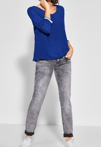 Blå långärmad topp med rundad halsringning och kontrasterande ljusblå detaljer. Kombinerad med ljusgrå avsmalnande jeans och vita sneakers.