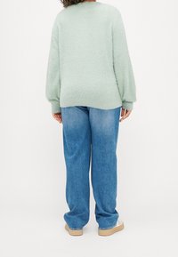 Ljust grönt fluffigt tröja med rundad halsringning, tillsammans med lösa blå denimjeans och beige sneakers. Strukturerad tyg och avslappnad passform.