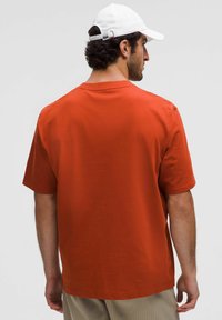 Camiseta de manga corta de color óxido hecha de tela suave. Presenta un ajuste relajado y un escote redondeado, con una textura sutil y suave y detalles mínimos.
