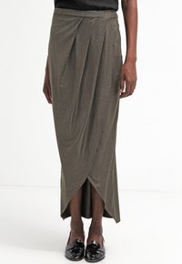 Lång, olivgrön kjol med metallisk lyster, med en draperad design och en omslags siluett, i kombination med svarta, blanka loafers.