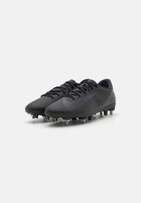 Scarpe da calcio nere con superficie texturizzata, caratterizzate da un design aerodinamico e una forma curvata. Tacchetti in gomma per aderenza e trazione sul campo.