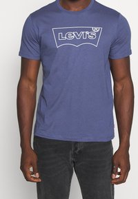 Pánské modré bavlněné tričko s bílou grafikou loga Levi's, kulatým výstřihem a krátkými rukávy. Hladká textura, volný střih.