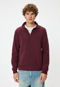 Bordeaux katoenen sweatshirt met een halve rits-kraag, geribde manchetten en zoom, en een ontspannen pasvorm, gecombineerd met lichtblauwe spijkerbroeken.