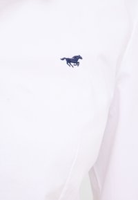 Biała bawełniana koszula z granatowym haftowanym logo konia na lewej piersi. Gładka tekstura o klasycznym kroju.