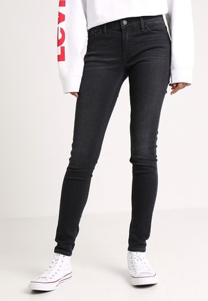 Jeans skinny negros de denim, con un clásico diseño de cinco bolsillos y costuras sutiles. Combinados con zapatillas blancas.