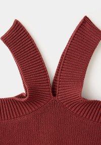 Gros plan d'un vêtement tricoté rouge rouille avec de larges bretelles côtelées formant un V sur un fond uni.