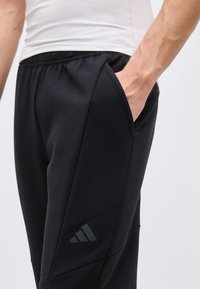 Κοντινό σε άτομο που φορά μαύρο παντελόνι Adidas με το χέρι στην τσέπη και λευκό εφαρμοστό πουκάμισο.