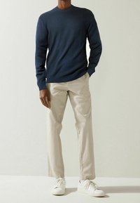 Pull en tricot bleu marine avec un motif texturé, associé à un pantalon beige et des baskets blanches, présentant un design minimaliste et des lignes épurées.