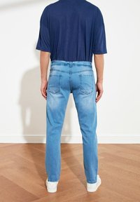 Jean en denim bleu clair avec une coupe droite, avec des poches arrière et une taille mi-haute. Associé à un t-shirt bleu marine foncé.