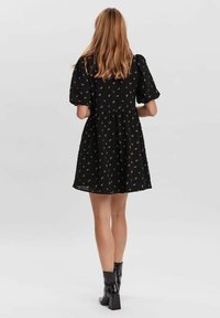 Schwarzes Kleid mit kurzen Puffärmelchen, strukturiertem Stoff, Blumenmuster, taillierter Taille und einem ausgestellt Rock. Mit einem gestuften Saumdetail.