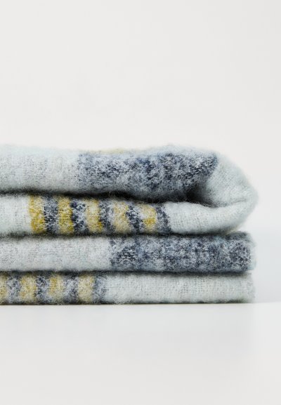 Stos trzech miękkich, teksturowanych koców w jasnoniebieskie, szare i żółte paski, wykonanych z puszystego materiału dzianinowego.