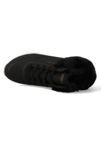 Zapatilla negra con cuello de piel sintética, parte superior texturizada, detalles perforados y cordones planos. Presenta una suela blanca contrastante y el logo de la marca.