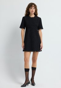 Musta, teksturoitu mini-mekko lyhyillä hihoilla ja fringed helmallä. Yhdistetty läpinäkyvien mustien polvisukkien ja teräväkärkisten korkokenkien kanssa.