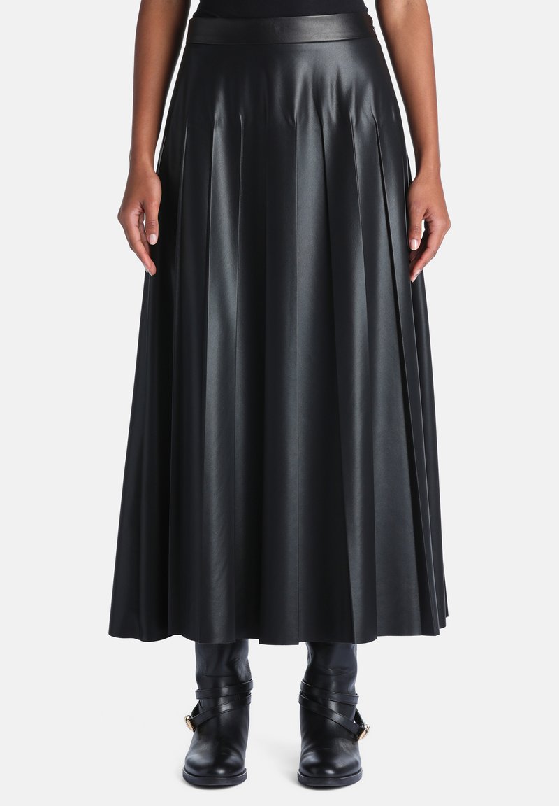 Jupe midi plissée en simili cuir noir portée avec des bottines noires et un top rentré, montrée de la moitié du torse jusqu'aux pieds sur un fond uni.
