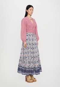 Rot-weißt gestreiftes, kürzes Bluse mit Puffärmeln, kombiniert mit einem langen, blumigen Rock in Blau und Pink, der einen dekorativen, kontrastierenden Saum aufweist.