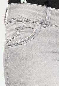 Šedé džíny z denimu s jemným vyblednutím, klasický pětikapsový design a viditelné švy podél švů a kapes.