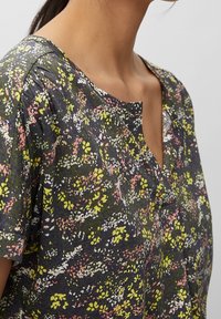 Bluse mit floralem Muster auf dunklem Hintergrund, verziert mit grünen, rosa und weißen Akzenten. Kurze Ärmel und runder Halsausschnitt. Weiche Stofftextur.