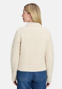 Sweter w kolorze kremowym, z teksturowanym ryżowym wzorem, z długimi rękawami i okrągłym kołnierzem, stylizowany z niebieskimi dżinsami.