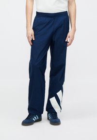 Αθλητικό παντελόνι σε ναυτικό μπλε χρώμα με ελαστική μέση και μεγάλο λευκό μοτίβο σε σχήμα βέλους. Κατασκευασμένο από ελαφρύ, υφασμένο ύφασμα.