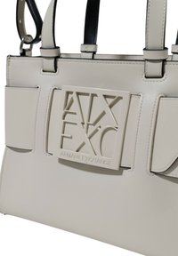 Borsa a mano grigio chiaro realizzata in materiale sintetico testurizzato. Presenta un design strutturato, doppio manico e una placca con logo ben visibile sul fronte.