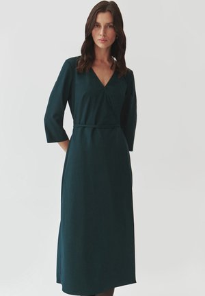 Dark green wrap dress with V-neck, 3/4 sleeves, waist tie, and a smooth texture, falling below the knee with a straight cut.
