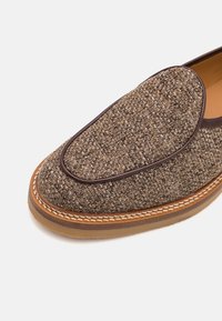 Hnědá tkaná slip-on obuv s texturovaným svrškem, koženým lemováním a kontrastní světlejší podrážkou. Obsahuje zaoblenou špičku a detailem prošívání.