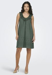 Zelena haljina bez rukava s čipkastim volanom na izrezu i cvjetnim vezom na rubu. Lagani, ležerni dizajn prikladan za toplo vrijeme.