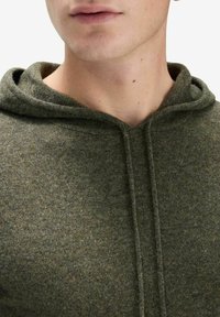 Olivgrön hoodie gjord av mjukt, strukturerat tyg. Har en huva med dragsko och en figurnära design, med släta sömmar och inga synliga logotyper.