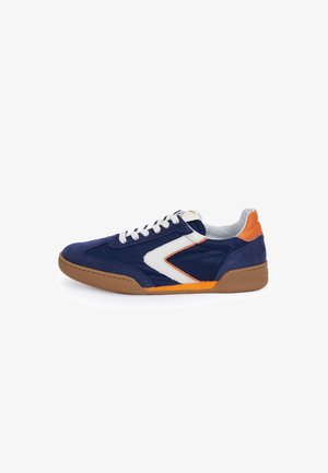 Lage sneaker met marineblauw textiel en suède, witte en oranje accenten, witte veters en een gumrubberen zool op een witte achtergrond.
