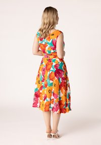 Blumenkleid mit lebendigen orange, roten und türkisfarbenen Mustern. Ärmelloses Design, taillierter Schnitt, fließender Stoff, knie-langer Saum.