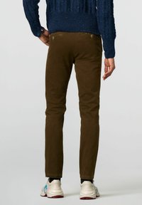 Slim-fit bruine chinos van katoen met een gladde textuur, voorzien van achterzakken met knoopsluitingen, gecombineerd met witte sneakers.