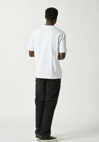 Vit bomullströja med rundad hals och korta ärmar, tillsammans med svarta byxor och bruna sneakers. En enkel, avslappnad passform.
