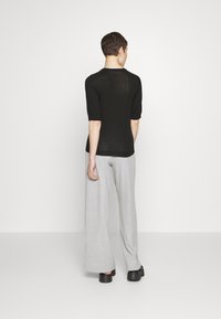Black knit pullover with short sleeves, paired with light gray wide-leg trousers and black platform shoes, viewed from the back.