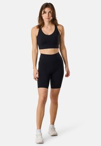 Svart sport-bh med rundad halsringning, kombinerad med svarta högmidjade cykelshorts. Båda är tillverkade av en mjuk, elastisk tyg.